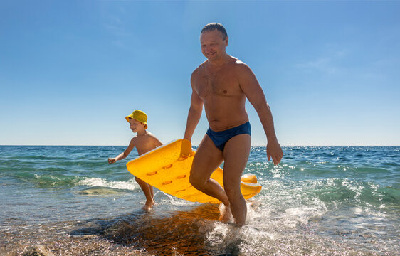 Father and son carry a yellow mattress on the beach