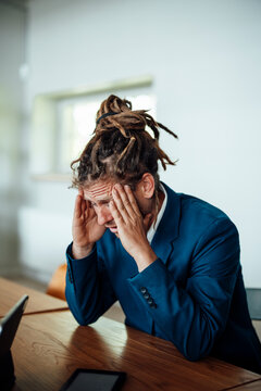Exhausted businessman with dreadlocks sits at his office desk