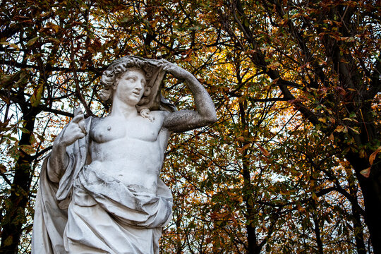 Stone statue stands beneath autumn foliage in the Tuileries Garden in Paris France surrounded by warm seasonal colors and mature trees