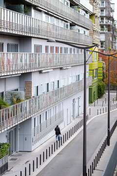 Residential balconies line a long apartment building in Paris France with a pedestrian walking through this quiet urban housing scene