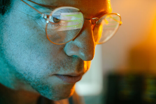 Male programmer looks at computer screen reflecting in his eyeglasses