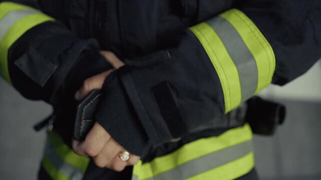 Close-up of a firefighter's hands fastening the clasp of a protective jacket with reflective safety stripes.