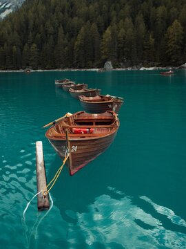 View of a wooden rowing boat moored on the turquoise waters of Lake Braies with a backdrop of dense pine forests in Prags, Trentino-Alto Adige, Italy.