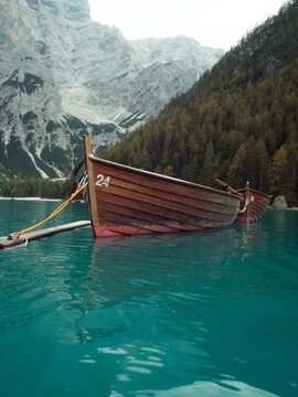 View of a wooden rowing boat on the turquoise water of Lake Braies with limestone mountains and pine forests in the background, Prags, Trentino-Alto Adige, Italy.