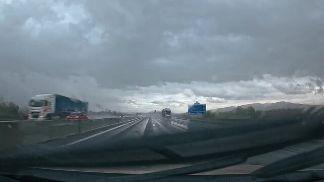 Trajet en voiture sur une autoroute de montagne sous la pluie et un ciel gris, avec une chauss&eacute;e d&eacute;tremp&eacute;e et les montagnes en arri&egrave;re-plan.