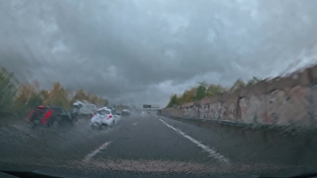 Trajet en voiture sur une autoroute de montagne sous la pluie et un ciel gris, avec une chauss&eacute;e d&eacute;tremp&eacute;e et les montagnes en arri&egrave;re-plan.