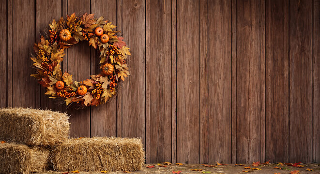 Autumn wreath hanging on a rustic wooden wall with hay bales in a cozy barn interior farm decor