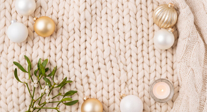 Knitted blanket with white baubles and green pine branch creating a cozy Christmas flat lay background