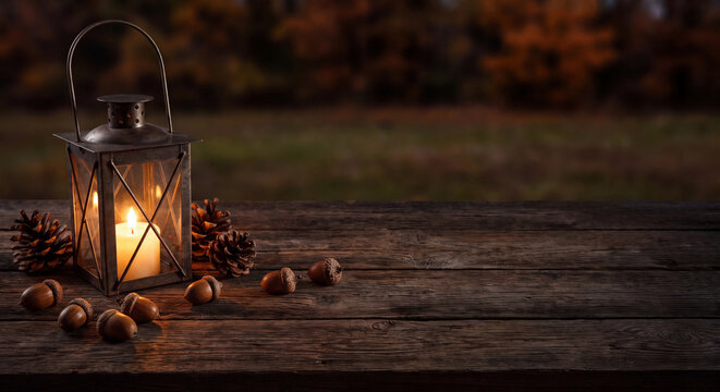 Vintage glowing lantern with a burning candle on a rustic wooden surface in a dark autumn evening setting