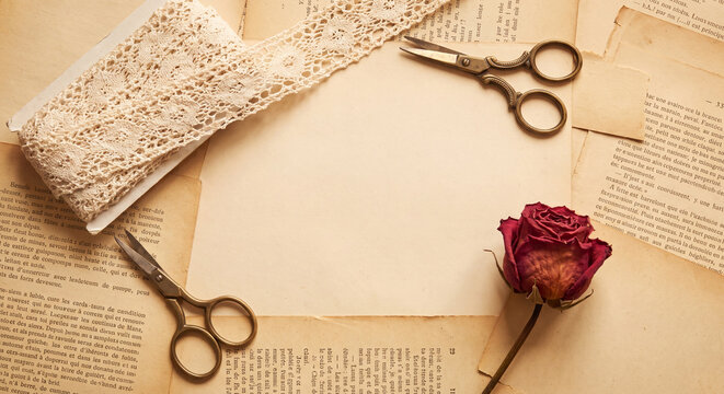 Vintage craft workspace featuring scissors with antique lace ribbon dried rose and old paper background