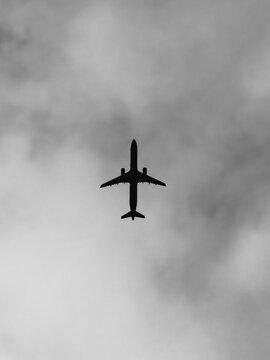 Airplane silhouette flying high through overcast cloudy sky view from below
