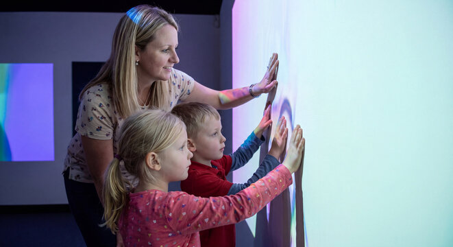 Mother and children touching interactive illuminated digital screen projection wall in modern museum
