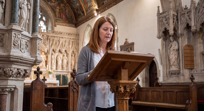 Woman speaker reading biblical verses from a wooden stand in a traditional gothic church