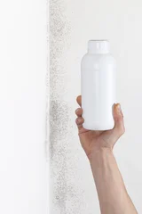 Hand holding blank white plastic bottle mockup near moldy wall for mold remover product concept © amedeoemaja
