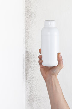 Hand holding blank white plastic bottle mockup near moldy wall for mold remover product concept