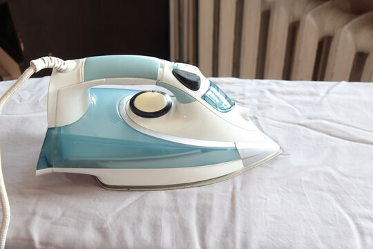 Close-up view of a steam iron resting on a blue shirt, illustrating garment care, wrinkle removal, ironing and everyday household maintenance.