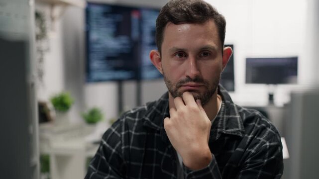 Caucasian male programmer thinking while looking at a computer screen in a modern office, software development and technology workplace concept.