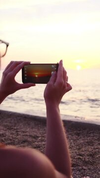 Over shoulder of female person at beach take photo of sunset