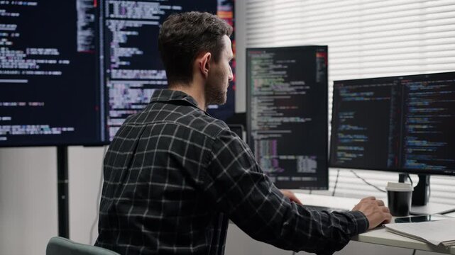 Caucasian male programmer developing software and reviewing code on multiple computer monitors in a modern office, technology and software development workplace concept.