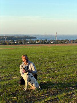 Man sitting with dalmatian dog on green field countryside landscape sunset