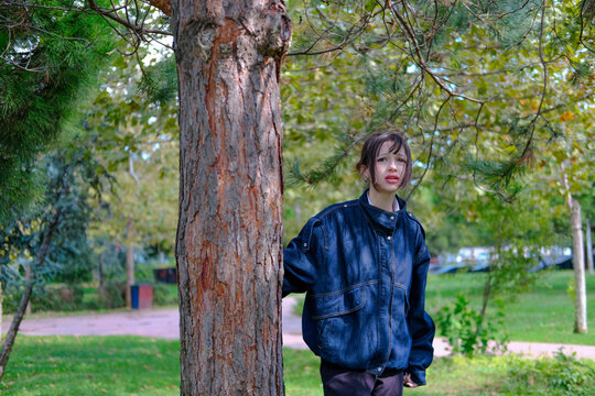 Young woman standing beside large tree trunk in autumn park looking up thoughtfully, contemplation, nostalgia, daydreaming, solitude, peaceful walk, nature connection and relaxation concept, copy spac