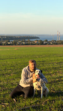 Man sitting with dalmatian dog on green field countryside landscape sunset