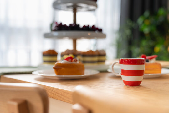 Coffee break and bakery cafe dining concept, red and white striped espresso cup on wooden table with fruit waffles and dessert tower softly blurred in background, symbolizing gourmet brunch.