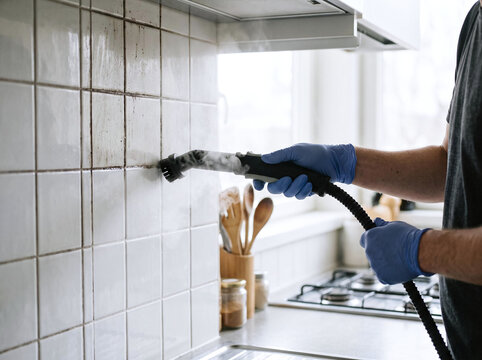 Person using a hot steam cleaner to clean dirty kitchen tile wall and grout
