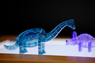 Translucent blue plastic dinosaur puzzle glowing softly on a light table representing creativity and childhood learning © Kamil