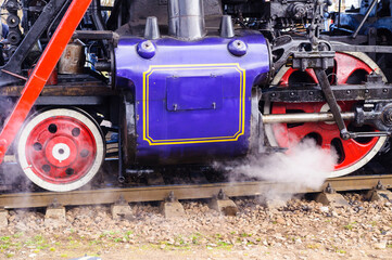 Railway background with a purple steam locomotive body and red driving wheels releasing white steam onto the tracks below © syntheticmessiah