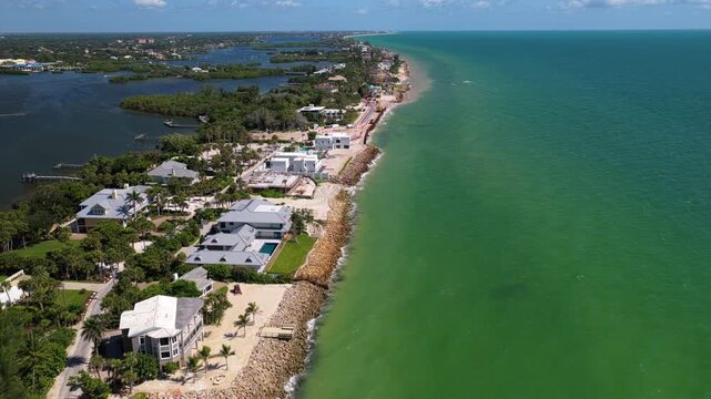 An aerial view follows a narrow, developed coastline with houses and a road between open water and wooded inland waterways.
