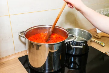 Cooking tomato sauce in big cooking pot, cooking italian kitchen home preserves, home canned food tomato sauce and wooden spoon, pan of tomato sauce © Pavlo Vakhrushev