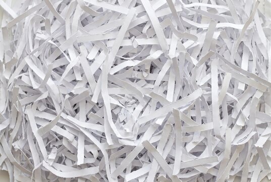 Overhead close up of white shredded paper strips. Cut document waste texture for data destruction, office recycling, and craft packaging background