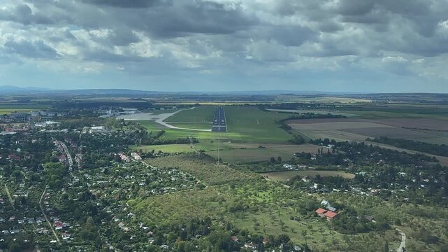 An immersive pilot view in a real time final approach to a short isolated runway surrounded by green fields under a partially clouded sky.