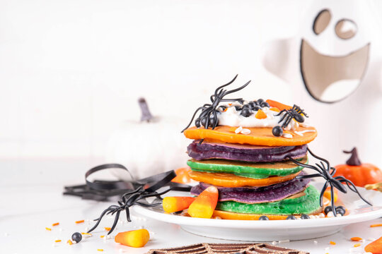 Colorful Halloween Pancakes with candy, pumpkin spider decoration. Stack of bright colored pancakes, with whipped cream, ready for Halloween breakfast or brunch