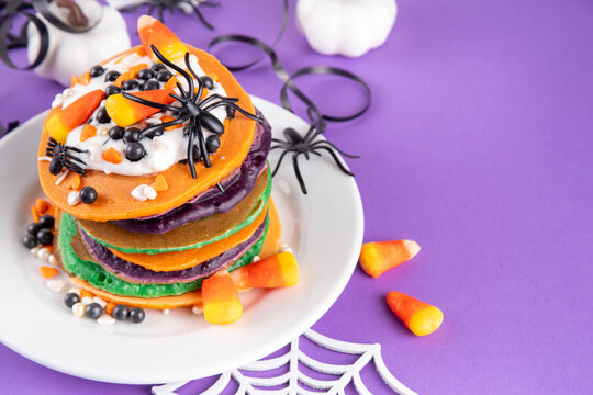 Colorful Halloween Pancakes with candy, pumpkin spider decoration. Stack of bright colored pancakes, with whipped cream, ready for Halloween breakfast or brunch
