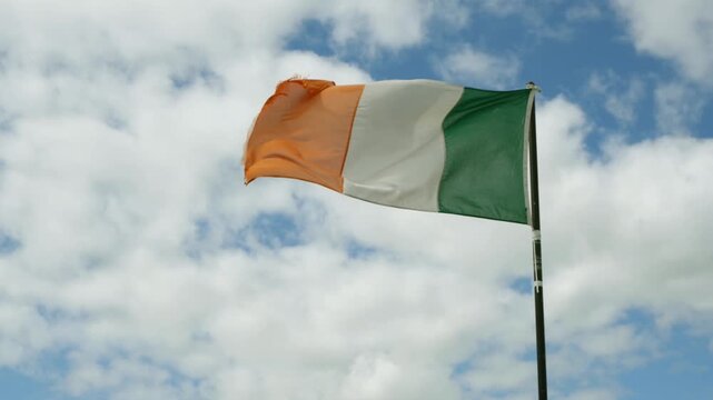 A slightly tattered Irish flag flutters gracefully against blue sky with clouds. Irish flag video