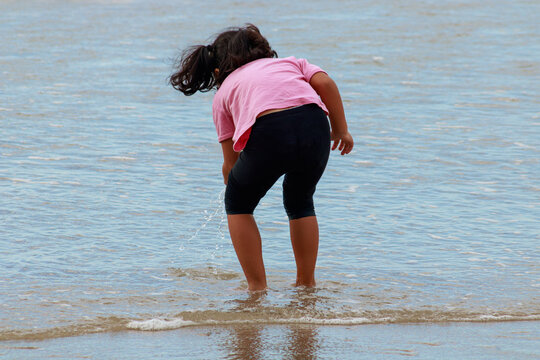 Child bends to splash in shallow ocean waves