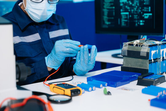 Expert technician testing a lithium-ion battery cell with a multimeter in a modern lab. Concept of renewable energy