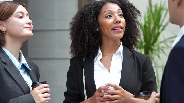 A professional team gathers outdoors during a break to discuss work projects while holding coffee cups. The colleagues communicate and share ideas, building connection and trust.