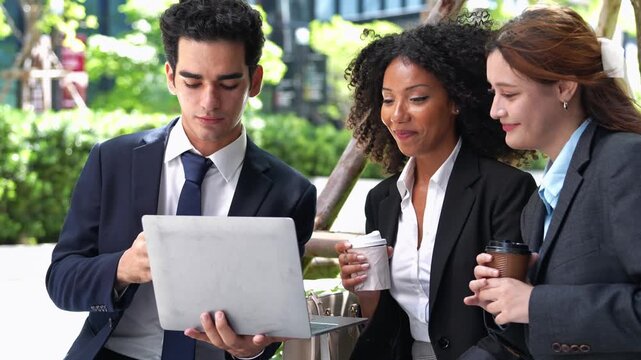 A professional business team gathers outdoors to review project data on a laptop together during a break. The group collaborates closely, sharing ideas and building strong trust.