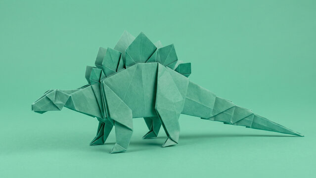 Green origami paper stegosaurus dinosaur on a matching green background