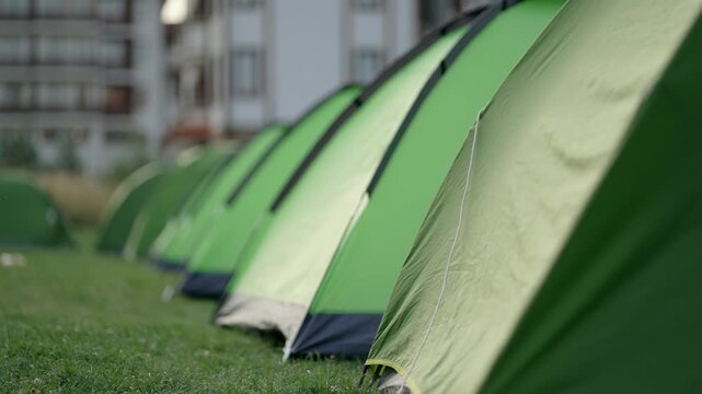 A row of green tents are lined up in a camping field. The tents are all the same size and color, and they are all set up in a row. The scene gives off a sense of organization and order