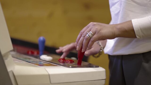 A woman is playing an arcade video game and pressing a red button and moving joystick