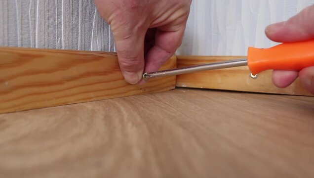 Person driving a screw with a screwdriver to secure the baseboard
