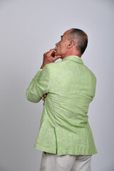 Naklejka premium Rückansicht eines älteren Mannes im hellgrünen Sakko mit nachdenklicher Hand am Kinn. Best Ager, Charakterporträt, Sommermode, Gentleman-Stil, Persönlichkeit und moderne Studiofotografie.
