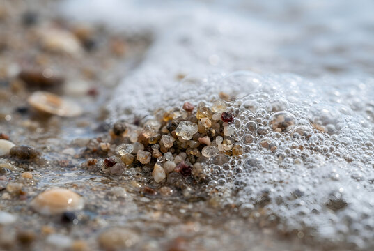 Macro View of Tiny Sand Grains Emerging From Sea Foam on a Beach