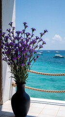 Fototapeta premium Purple flowers in black vase sit on balcony with sea view. Tropical blossoms decorate tiled terrace near ocean. Small boats float on turquoise water under clear blue sky. Peaceful summer vacation at