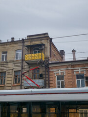 Historic urban building facades with ornate windows, rooftop chimneys, overhead utility wires, yellow balcony panels, and modern tram roof in European city street © Denis Tuev