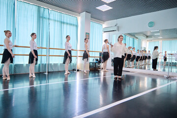 Female ballet coach guides young dancers across bright studio floor © TRAVELARIUM